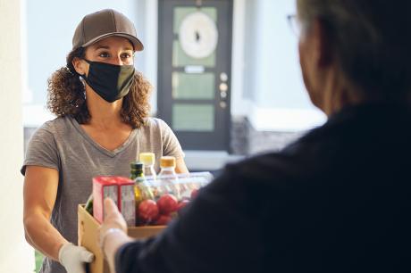 A woman wearing a mask delivering groceries.