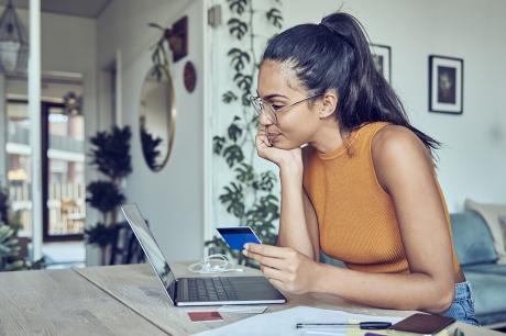 A young woman looking at a laptop in her home.