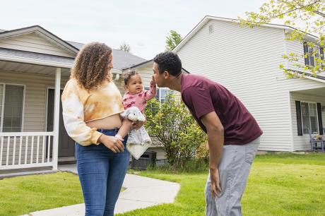 A young couple and their baby in front of their home.