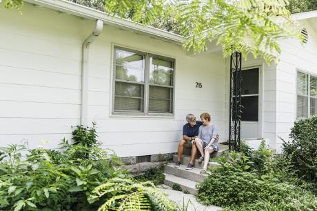An older couple sitting on the steps of a single family home.