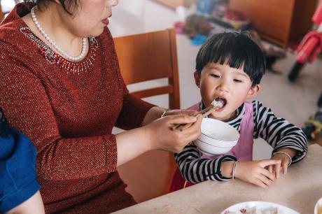 A woman feeding a younger boy some rice.