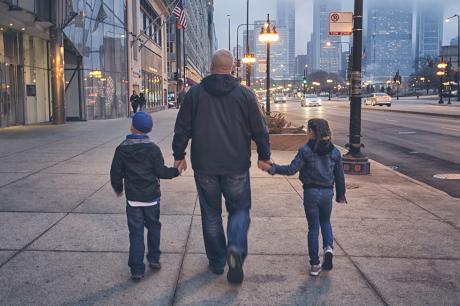 photo of father holding hands with children walking on sidewalk