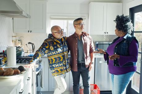 photo of male couple in kitchen talking to another person