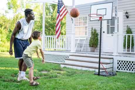 photo of father playing basketball with child outside of house