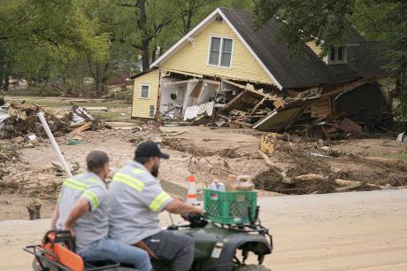 Men on a four wheeler pass a storm-damaged house along Mill Creek in the aftermath of Hurricane Helene on September 30, 2024, in Old Fort, North Carolina.