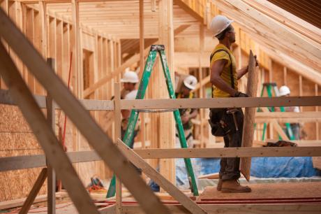 photo of Hispanic carpenters bringing sheathing to roof at a house under construction