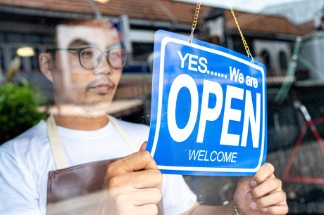 A worker hanging a sign indicating that they are open. 