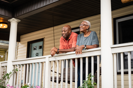 An image of an older couple on the front porch of their house.