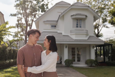 A couple hugging each other outside a single family home. 