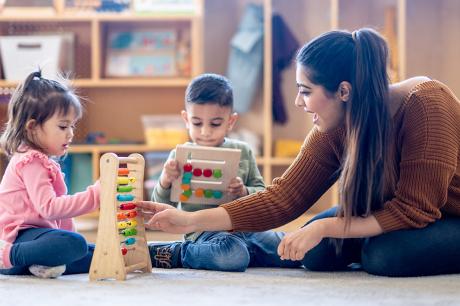 A teacher playing with blocks with two younger children.