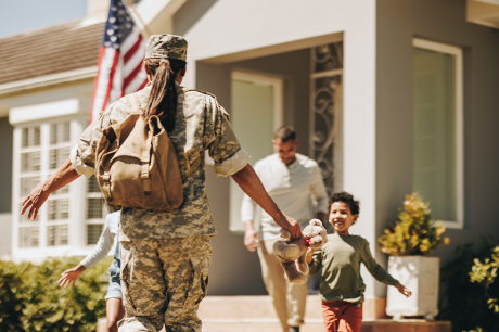 Photo of a young army veteran returning home to her family. She extends her arms to her children as they run towards her.