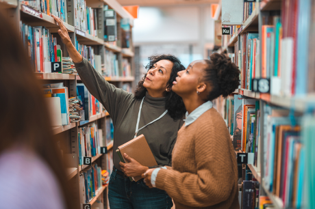 Two women in a library looking at books.