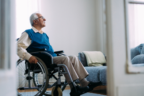An older man in a wheelchair looks out his window.