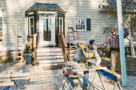 Photo of two construction workers repairing the siding around a house's back door. 