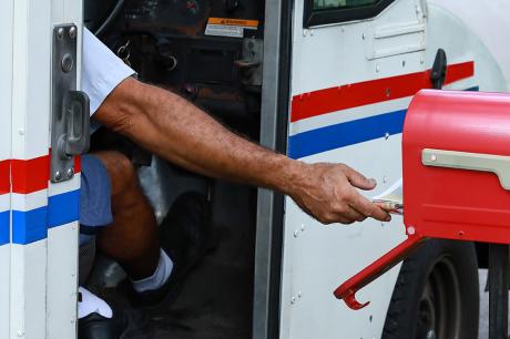 photo of mail worker putting letter in mailbox