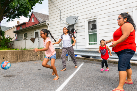 An immigrant family—three children and their mom—playing with a ball outside.