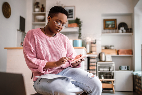 Photo of a young Black woman in a pink sweater reviewing her finances.