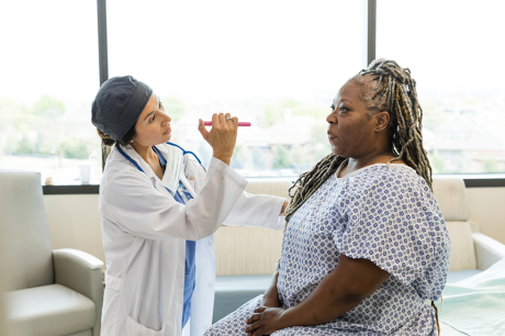 Photo of an older Black woman in a hospital gown having her vitals checked.