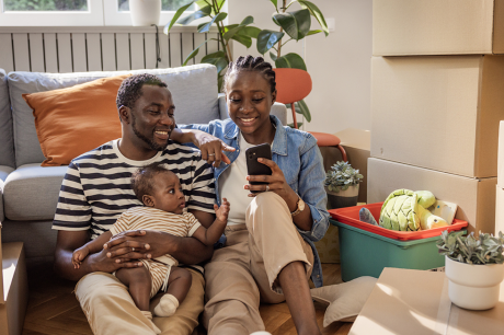 Two parents and their child sit among moving boxes in a new home.