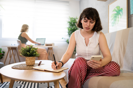 Image of a young white woman checking her phone and writing something down. 