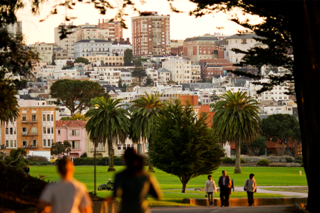 Two people running through a park in San Francisco with apartment buildings and other housing types in the background.