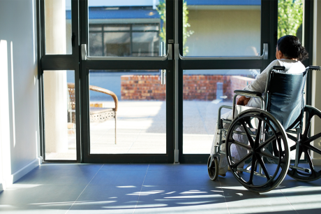 Photo of a woman in a wheelchair looking outside the glass doors of a medical facility. 
