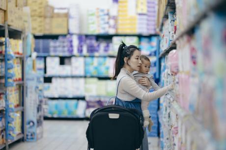 An Asian mother and daughter are selecting baby products at a shopping mall. The mother holds her child in her arms, carefully inspecting the material and quality of the items to choose the most suitable products for her baby.