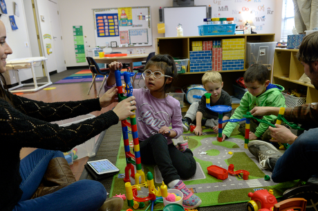 Three young children play with child care providers