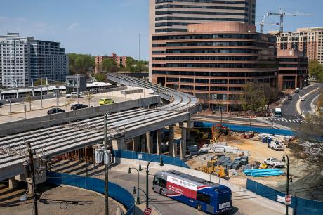 A bus drives under an underpass and beside a construction area