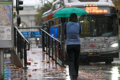 photo of a woman with umbrella waiting at a bus stop during rainy weather