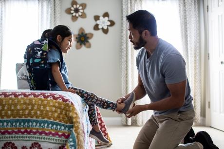 Photo of a father helping his daughter put on her shoes before school. 
