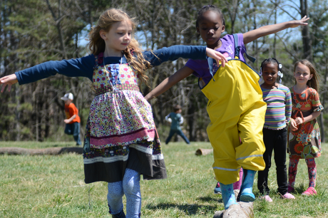 Two children play together outside, one walks on a balance beam