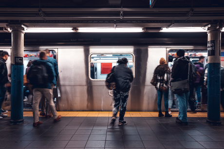 People hurry on and off a subway train at an underground station, with motion blur showing movement as doors stand open and passengers board and exit.
