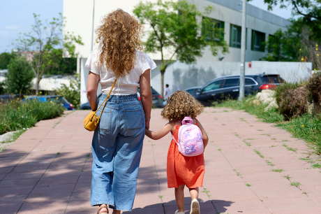 Photo of a mother walking her daughter to school on a sunny day. 