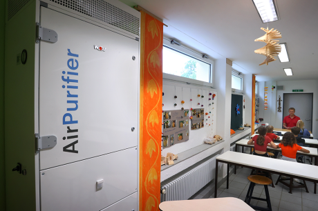 Classroom with students at tables and a large air purification unit installed along one wall.