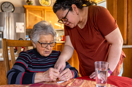 Photo of a direct care worker helping an older woman take a COVID test in her home. 
