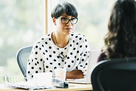Two people talk at a desk