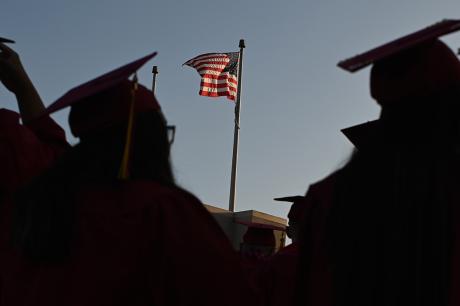 Students graduating from college stand in front of an American flag