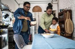Two parents and their child set the table for a meal in their kitchen