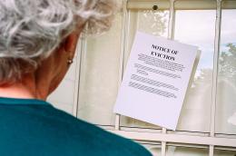 An senior woman with short grey hair reads a notice of eviction taped to her front door.