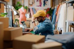 Man wearing a baseball cap looks at a laptop and holds his forehead 
