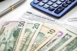 A calculator, a paper clip, a pen, a 1040 tax form, and a stack of dollar bills ranging from $50 to $1
