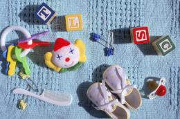 A photo of various baby items, including two small purple shoes, a baby comb, and a pacifier, arranged on a textured light blue blanket. 