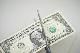 A close-up of a pair of scissors cutting an American $1 bill in half