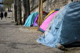 Four multicolored tents sit on a cobbled sidewalk along a street.