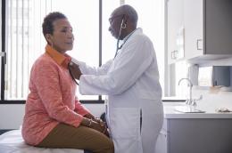 A doctor uses a stethoscope on a woman sitting on an exam table
