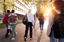 A group of students with backpacks strolls around a college campus as the sun comes up.