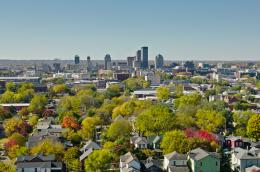 A high perspective shot overlooking a suburban neighborhood with lots of trees toward taller buildings downtown.