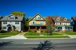 A streetview of three colorful multistory family homes on a sunny residential street.