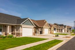 A sidelong view of several beige homes on a sunny residential street.